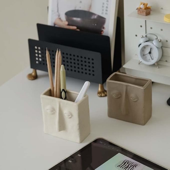 WENSHUO Ceramic Pen Holder, Pencil Holder for Desk, Desk Accessories, Crème | 3.7 in tall ceramic holder for pens, pencils, makeup brushes, or toothbrushes. Abstract face design displays small plants.